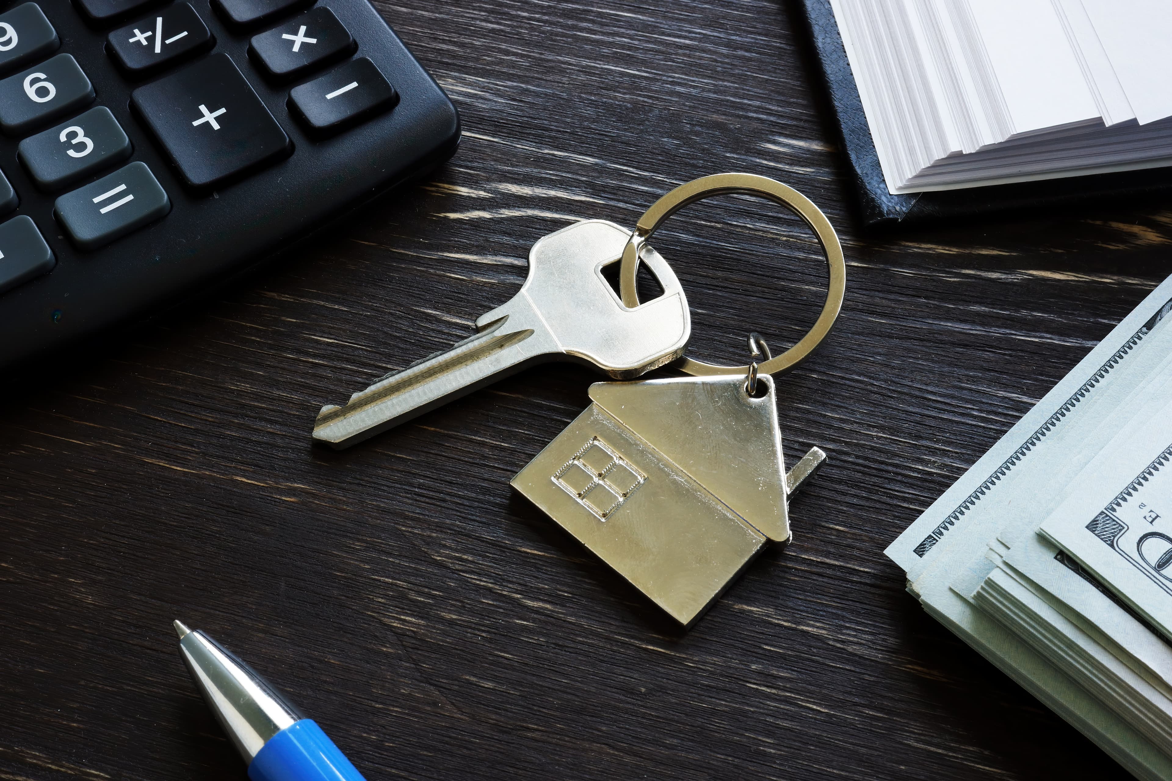 House key with keyring, calculator, and cash on a desk